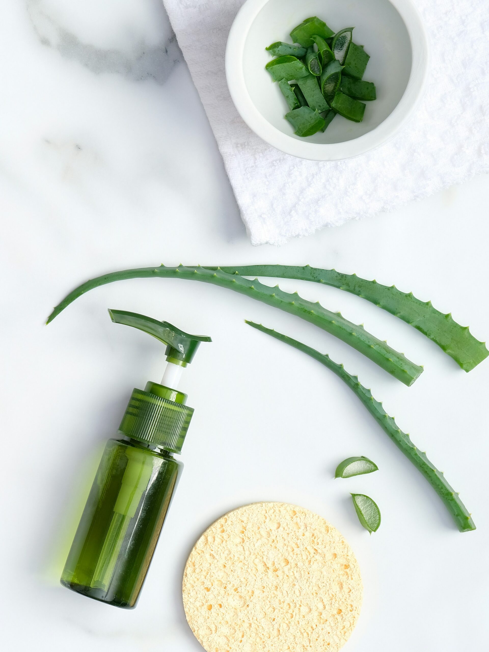 Flatlay van kalmerende skincare met aloë vera, een natuurlijke aloë vera plant en een spons