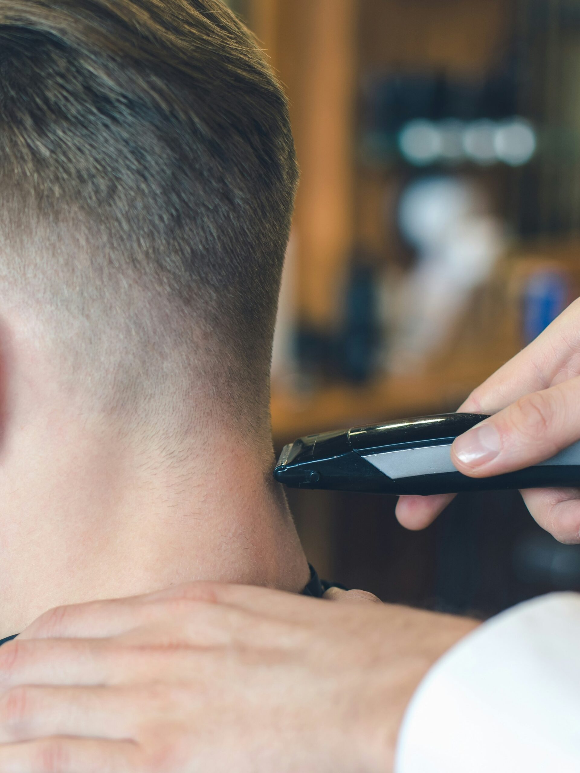 Close-up van een kapper die een taper fade knipt bij een klant met steil haar, met de tondeuse aan de achterkant van het hoofd