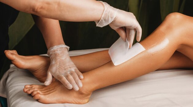 Close-up van een specialist die het onderbeen van een cliënt waxt in een lichte, schone salon