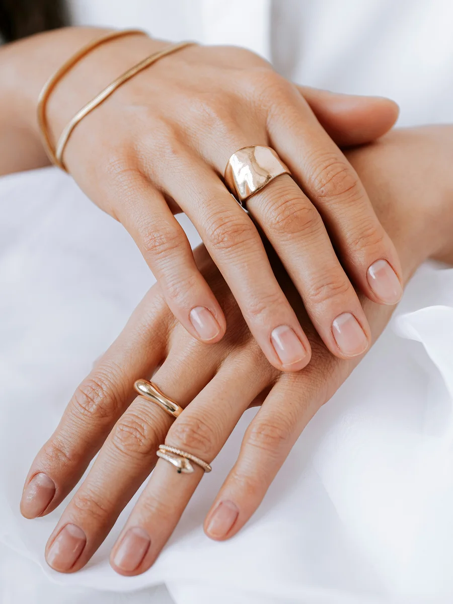 Close-up van twee handen op een wit laken met gezonde, natuurlijke nagels, gesierd met ringen en armbanden in roségoud