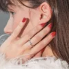 Close-up zijaanzicht van een brunette vrouw, met haar hand tegen haar gezicht en een glanzende rode gelmanicure