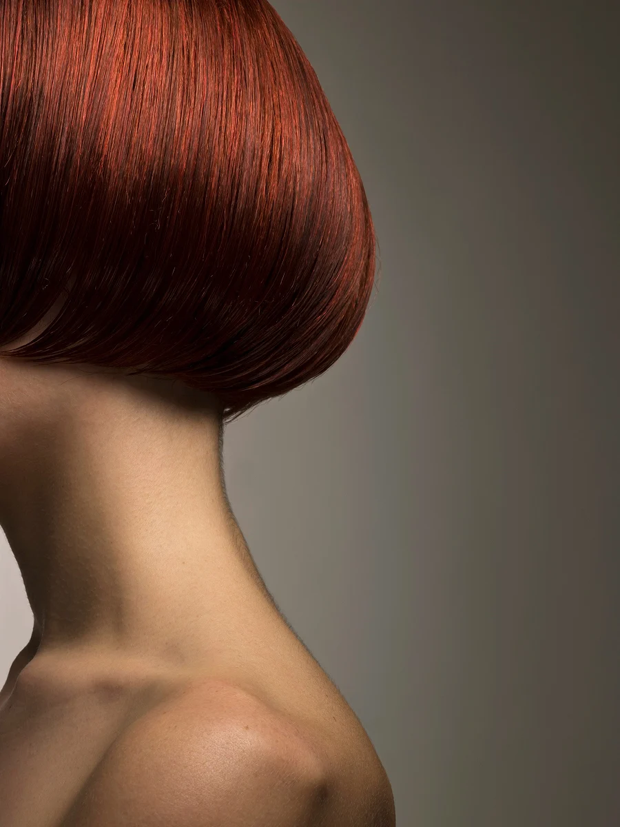 Close-up zijaanzicht van het hoofd van een vrouw met een glanzende, rood geverfde bob