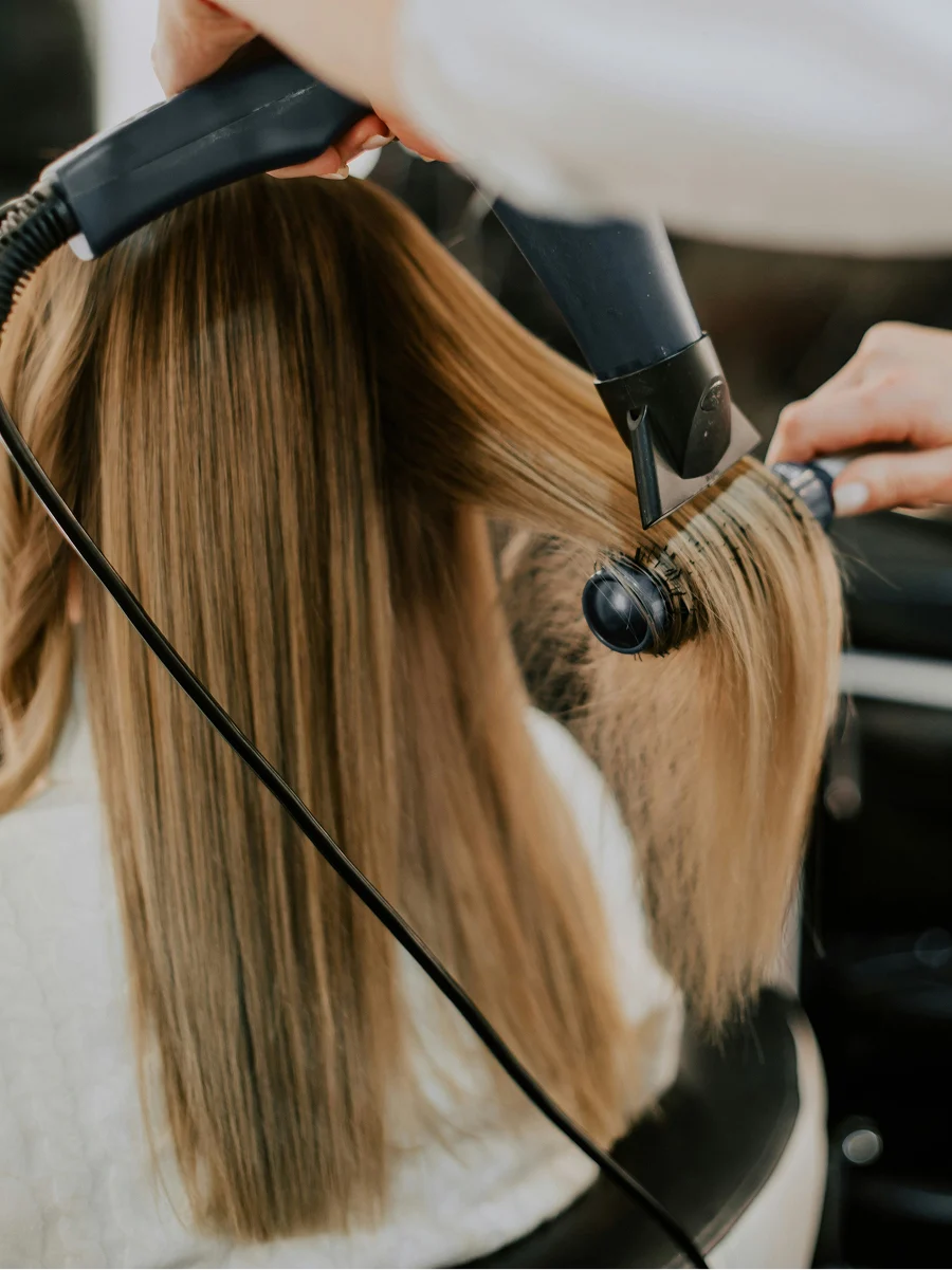 Achteraanzicht van een vrouw bij de kapper terwijl een stylist haar haar steil föhnt tijdens een keratinebehandeling