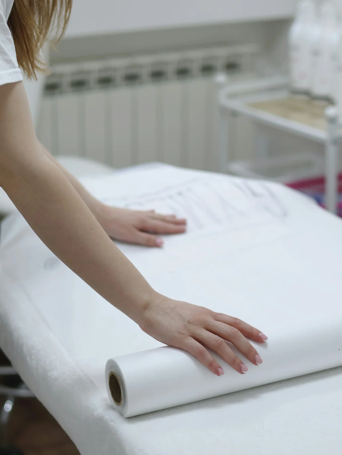 Close-up van de armen van een waxspecialist die een schoon vel papier over een behandeltafel uitrolt om een behandeling voor te bereiden