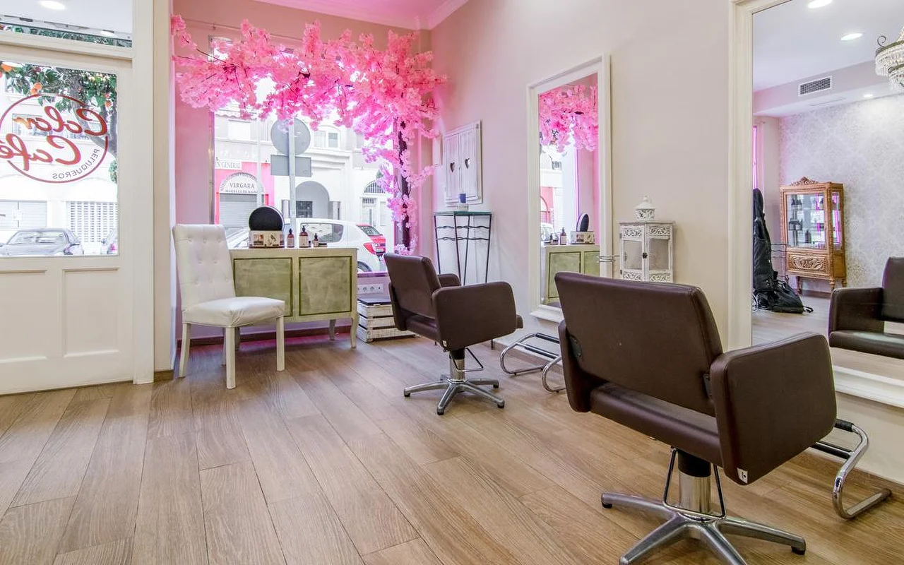 Het interieur van Color Café Peluqueros in Torremolinos, een kapsalon met roze muren, bruine stylingstoelen, grote spiegels en een roze kersenbloesem-decor in de etalage.